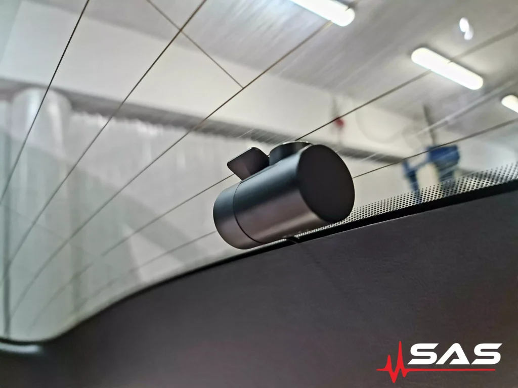 Tylny wideorejestrator zamontowany na szybie Forda S-Max. Kamera została zamocowana z największą starannością, aby zapewnić doskonały kąt widzenia i estetykę wnętrza. W tle widać detale warsztatu, które wskazują na profesjonalne podejście do instalacji.