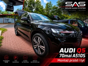 Czarny samochód osobowy zaparkowany przed serwisem audio, widoczna zainstalowana kamera samochodowa. Audi Q5 z zamontowanym wideorejestratorem.
