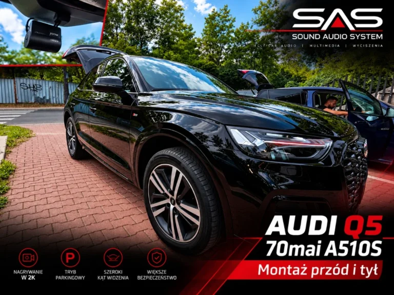 Czarny samochód osobowy zaparkowany przed serwisem audio, widoczna zainstalowana kamera samochodowa. Audi Q5 z zamontowanym wideorejestratorem.